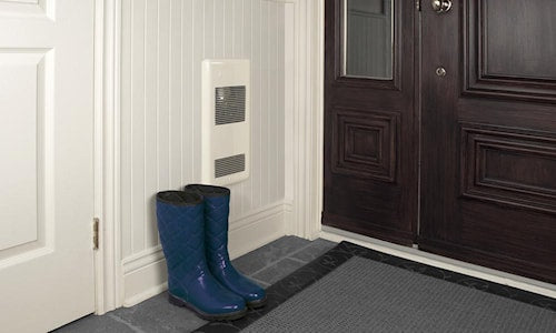 Chauffage mural électrique installé dans une entrée de maison, accompagné d’une paire de bottes bleues posées au sol près de la porte.
