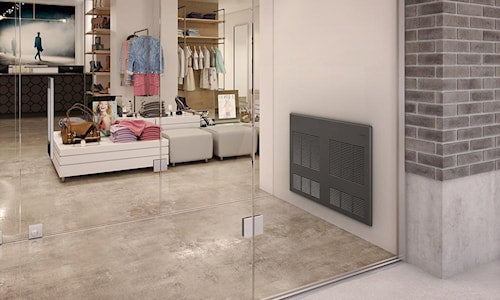 Chauffage mural gris installé dans une pièce moderne au plancher de béton, avec dressing vitré et mobilier blanc à l’arrière-plan.