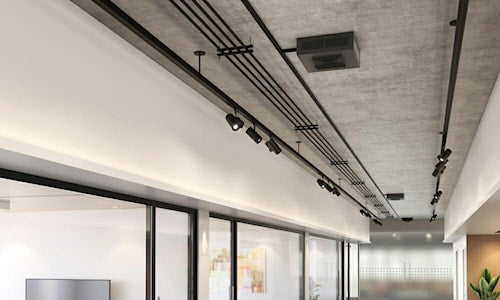 Intérieur de bureau moderne avec plafond en béton apparent, conduits électriques visibles et système d’éclairage sur rail