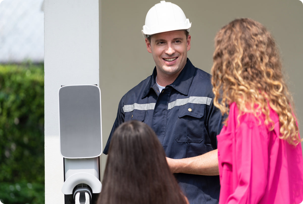 Technicien souriant échangeant avec des clients devant une résidence, dans le cadre d'un projet d'installation électrique.